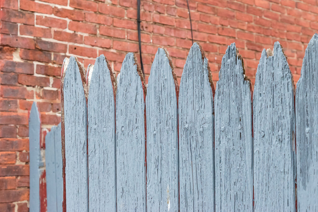 Fence with cracked blue paint with a background of red brick.