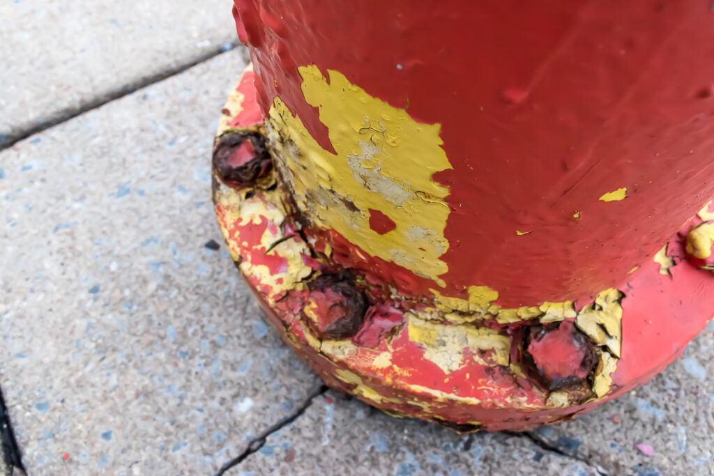 Peeling red and yellow paint on the base of a fire hydrant